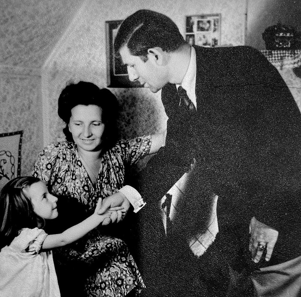 Family photo, black and white: father, mother and a little girl, all festively dressed. The father shakes the girl's hand, Munich 1949 © Private collection