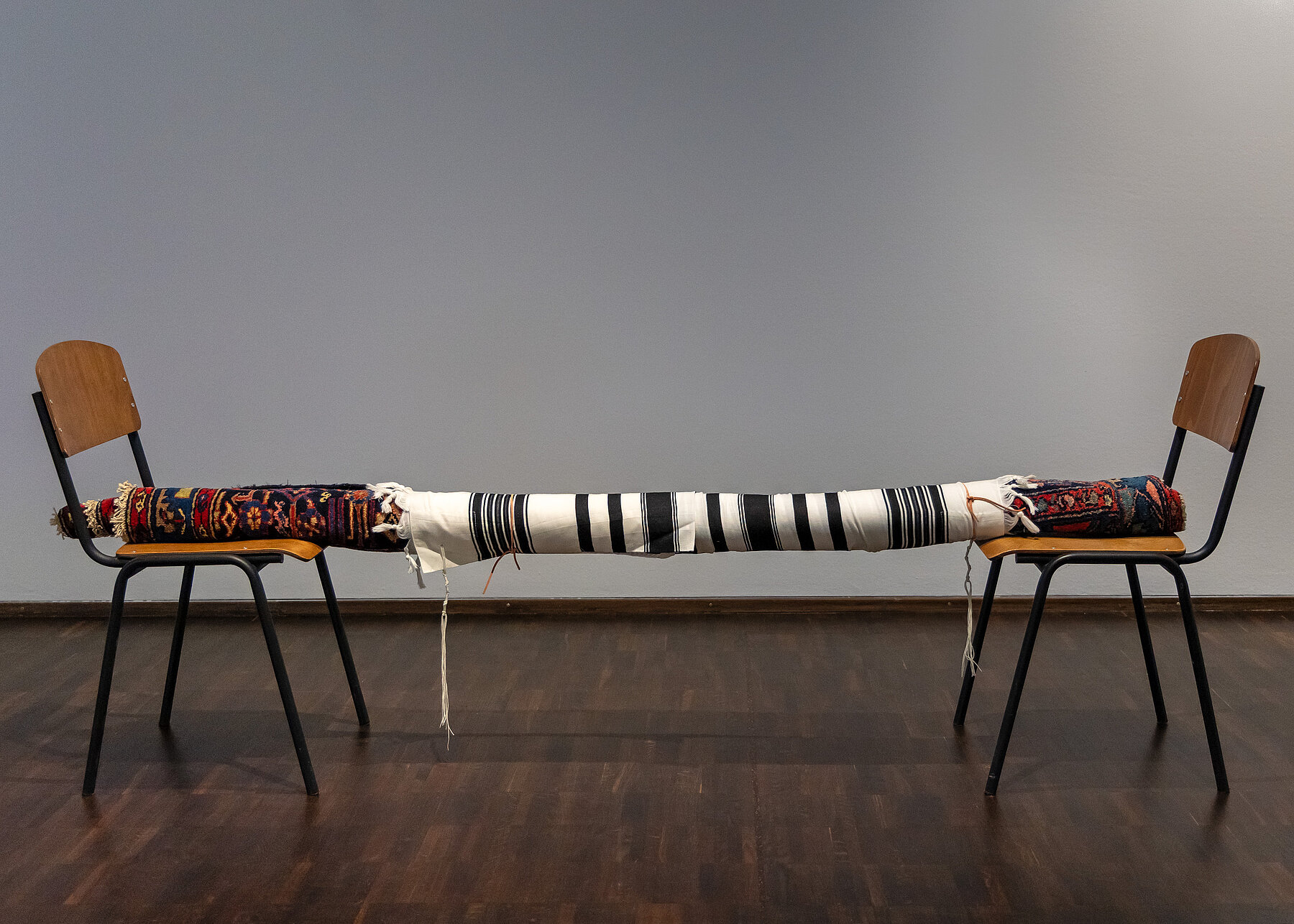 A carpet, a prayer shawl and a leather strap suspended between two chairs 