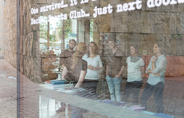 Blick durch die Glasfassade, dahinter Menschen im Museum bei einem Rundgang 