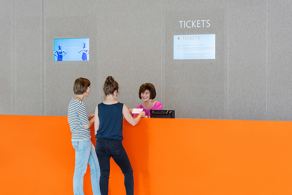 Zwei Besucher*innen kaufen an an der Kasse des Jüdischen Museums München eine Eintrittskarte, Foto: Daniel Schvarcz / JMM
