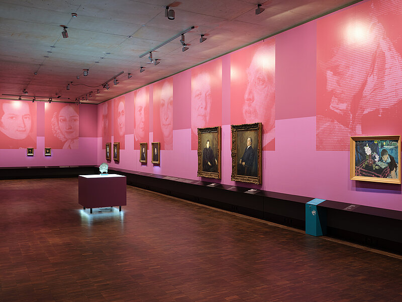 Ausstellungsansicht „Bildgeschichten. Münchner Jüdinnen und Juden im Porträt“ - mehrere Porträts hängen nebeneinander in einem Ausstellungsraum in Rosétönen, große Blowups spiegeln das Motiv der Bilder, Foto: Eva Jünger / Jüdisches Museum München 