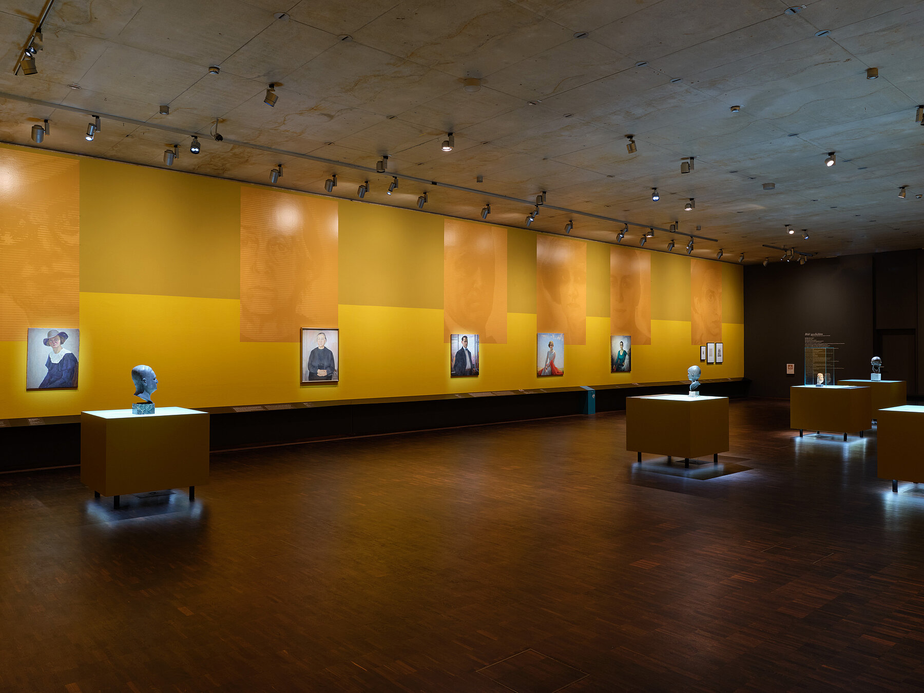 Ausstellungsansicht „Bildgeschichten. Münchner Jüdinnen und Juden im Porträt“ - mehrere Porträts hängen nebeneinander in einem Ausstellungsraum in Gelbtönen, große Blowups spiegeln das Motiv der Bilder, Foto: Eva Jünger / Jüdisches Museum München 