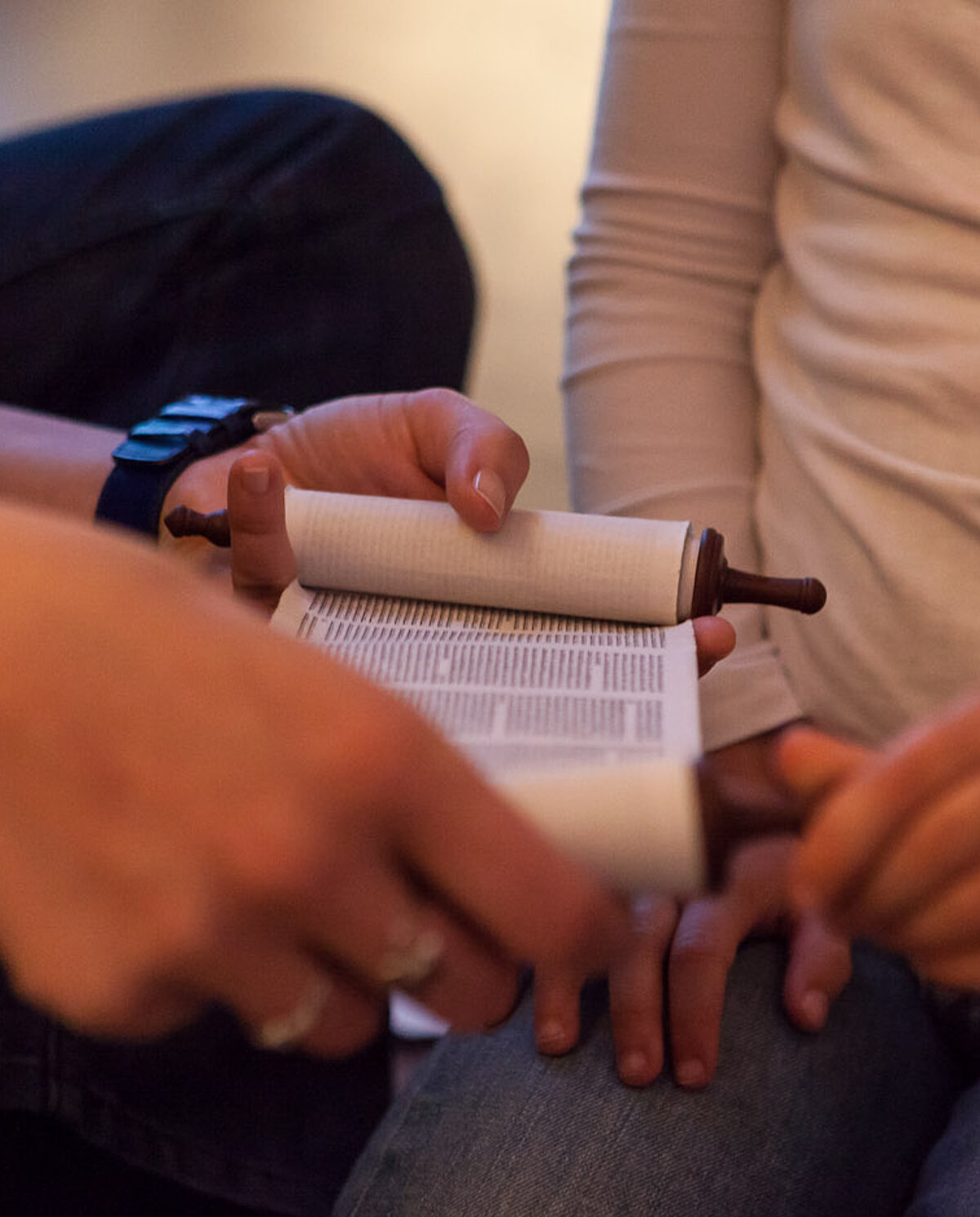 Eine Besucherbetreuerin sitzt in der Dauerausstellung neben einem Kind und zeigt eine kleine Thorarolle. 