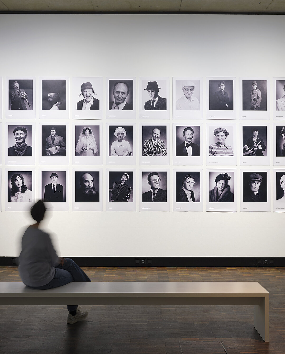 Ausstellungsansicht „Die Dritte Generation. Der Holocaust im familiären Gedächtnis“, mit Rafael Goldchain "I Am My Family", davor sitzend eine Besucherin. Foto: Eva Jünger / Jüdisches Museum München 