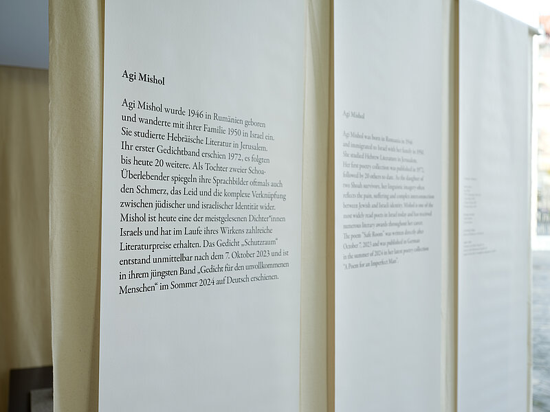Installation view "October 7" a text panel hanging from the ceiling with the biography of Agi Mishol, photo: Eva Jünger / Jewish Museum Munich
