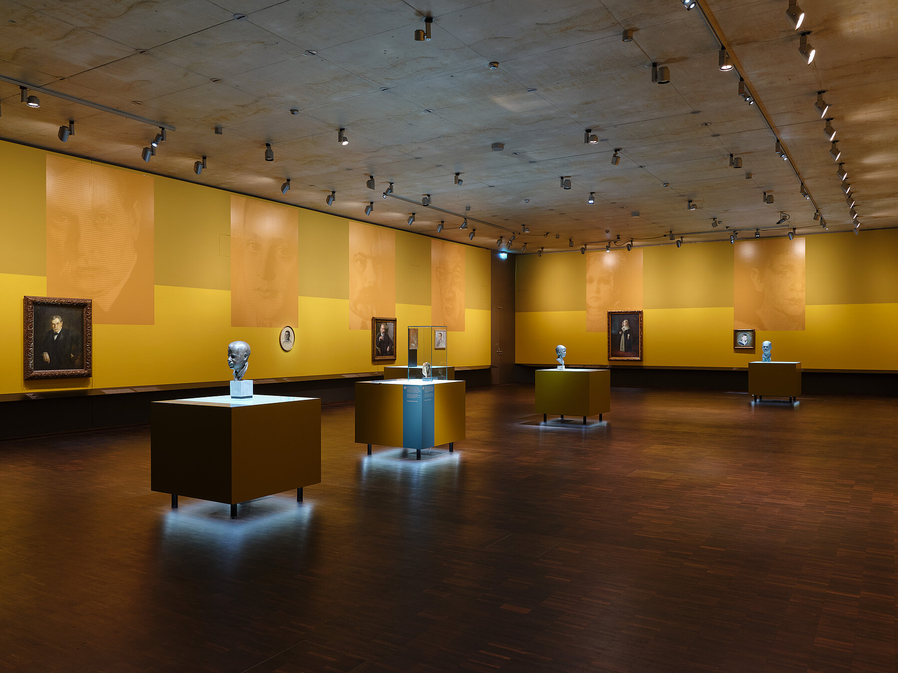 Ausstellungsansicht „Bildgeschichten. Münchner Jüdinnen und Juden im Porträt“ - mehrere Porträts hängen nebeneinander in einem Ausstellungsraum in Gelbtönen, große Blowups spiegeln das Motiv der Bilder, Foto: Eva Jünger / Jüdisches Museum München 