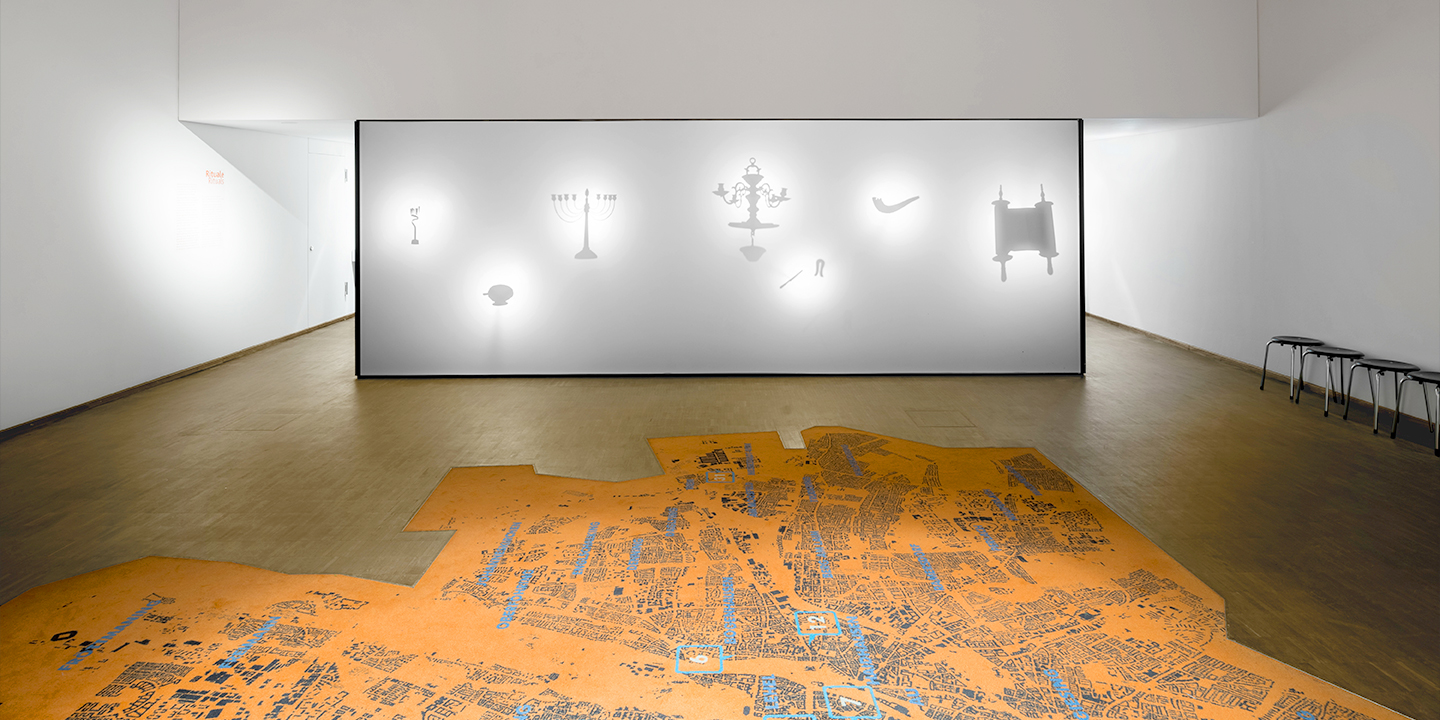 Installation ORTE in der Dauerausstellung: eine Schattenwand lässt verschiedene jüdische Ritualgegenstände erahnen © Daniel Schvarcz